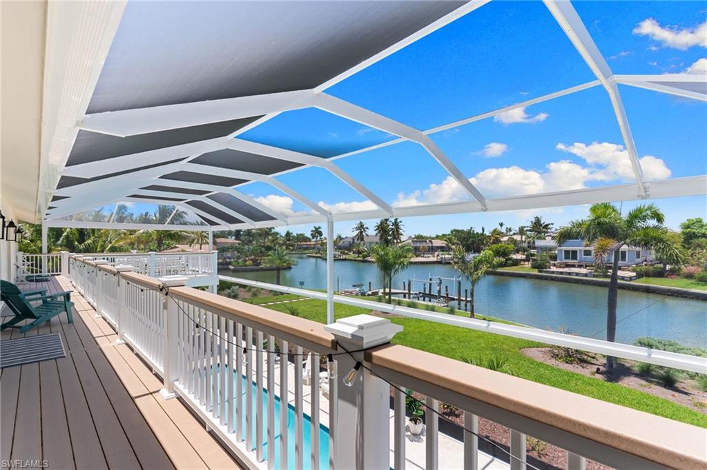 Screened outdoor living area with composite decking and white railing, overlooking a canal with lush landscaping and a swimming pool