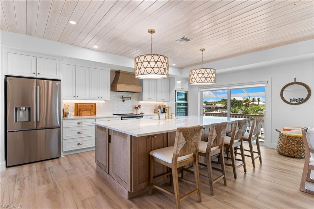 Gourmet kitchen featuring a large island with seating, stainless steel appliances, white cabinetry, and wood-finish flooring