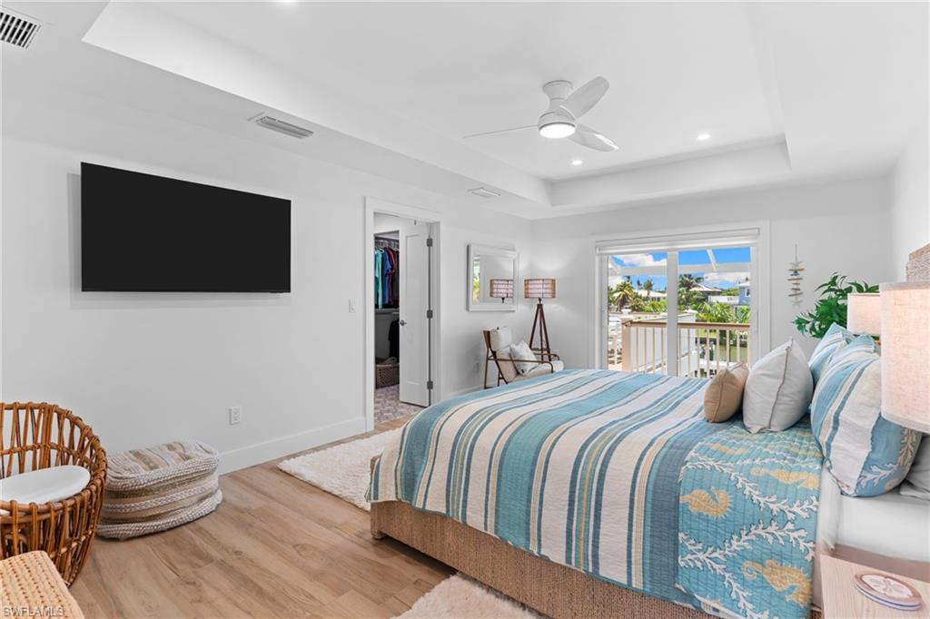 Spacious room featuring wood-finish flooring, a tray ceiling with recessed lighting and a ceiling fan, and sliding glass doors opening to an outdoor balcony