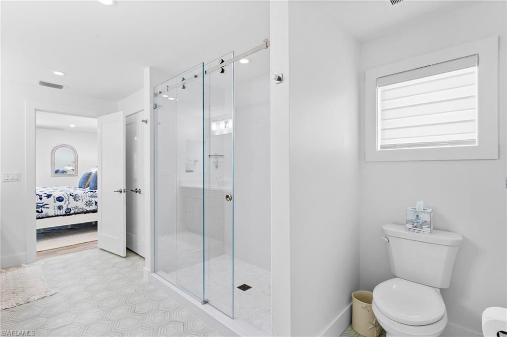 Bathroom featuring a glass-enclosed shower with sliding doors, a white toilet, and a window with privacy blinds