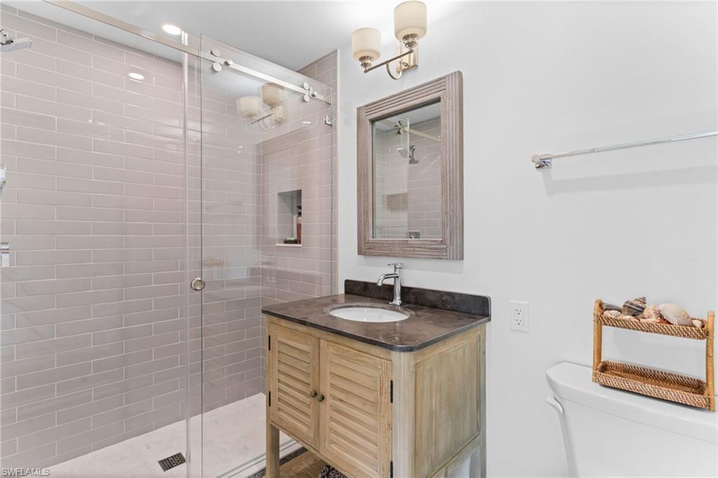 Spacious bathroom featuring a glass-enclosed shower with subway tile, a built-in shower niche, and a vanity with a dark countertop and undermount sink