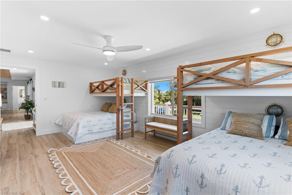 Bright room featuring two built-in bunk beds with natural wood frames, wood-finish flooring, white shiplap wall accents, and recessed lighting
