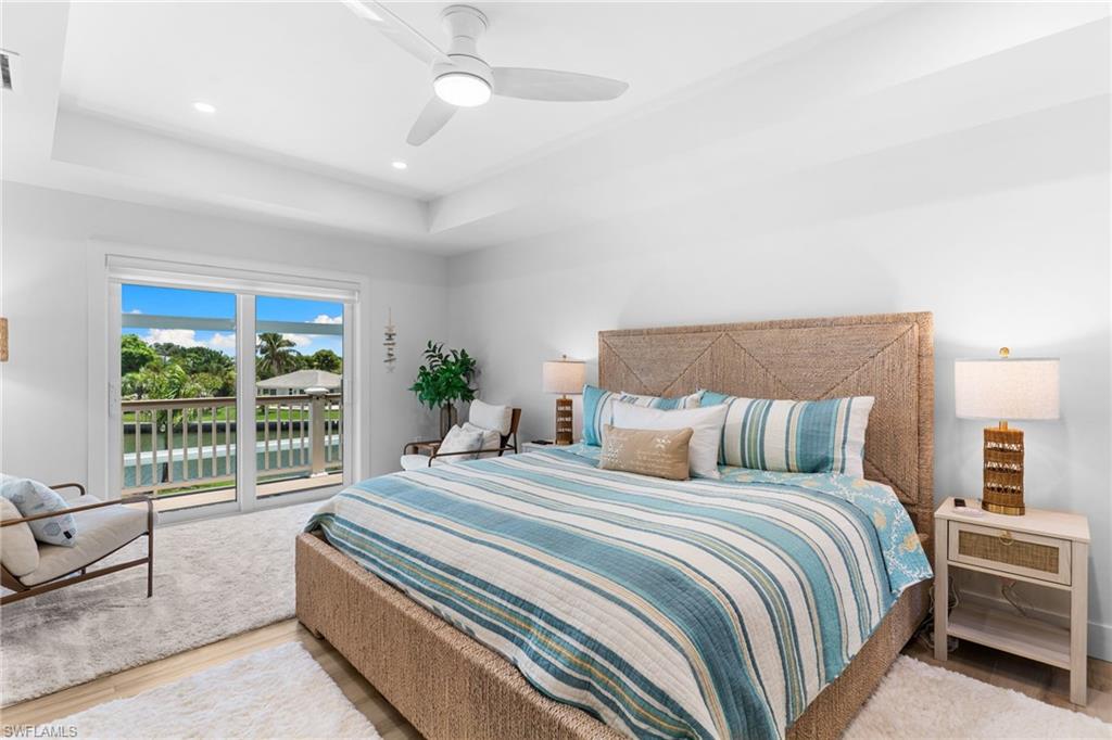 Bright room with tray ceiling and recessed lighting, featuring sliding glass doors opening to a balcony with water frontage