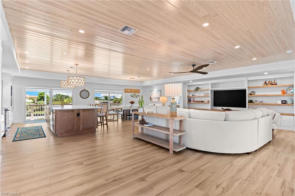 Spacious open-concept living area featuring wood-finish flooring, a shiplap ceiling with recessed lighting, and a built-in media center with shelving