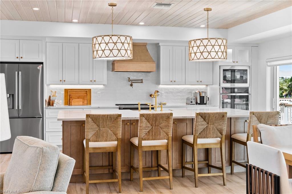 Modern kitchen featuring a large central island with seating, white shaker cabinetry, stainless steel appliances, and a wood-finish shiplap ceiling