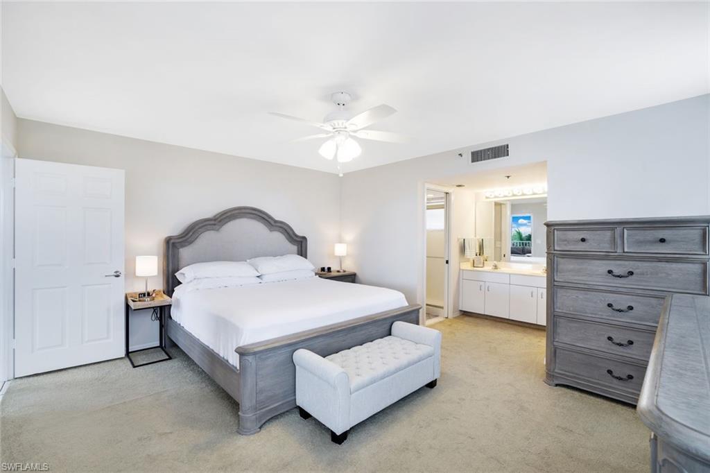 Bedroom with ceiling fan, light colored carpet, and ensuite bath