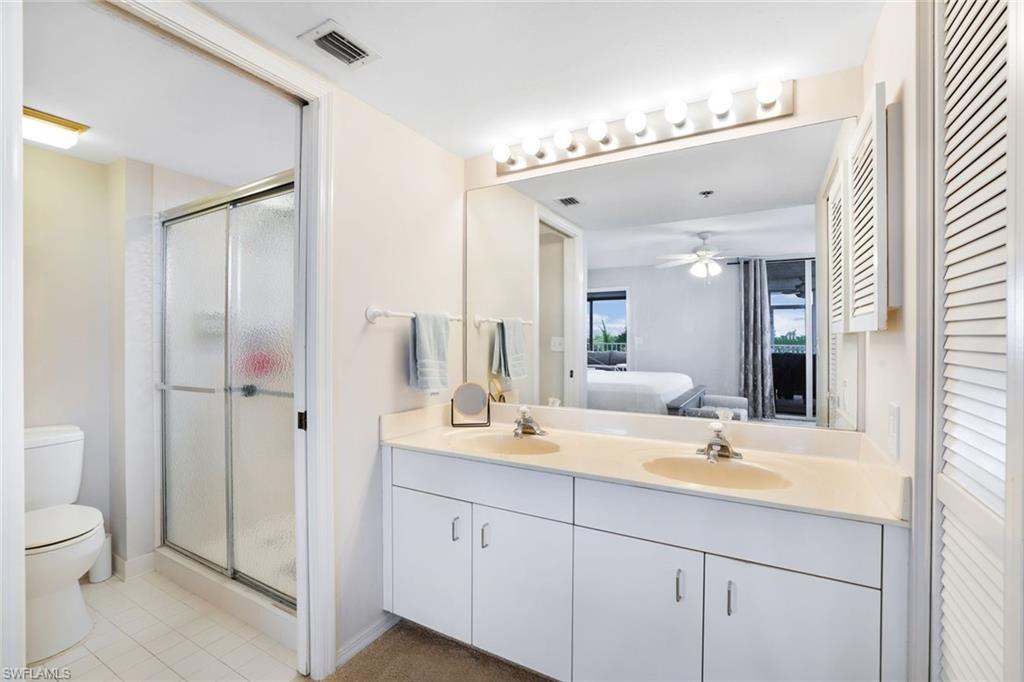 Bathroom with dual vanity, ceiling fan, toilet, tile floors, and walk in shower