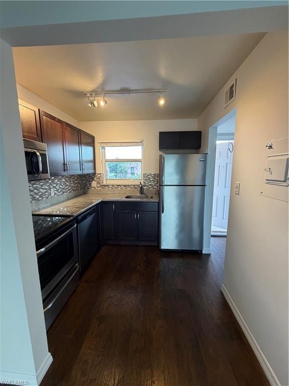 Kitchen featuring wood-finish flooring, dark cabinetry, stainless steel appliances, and a tiled backsplash