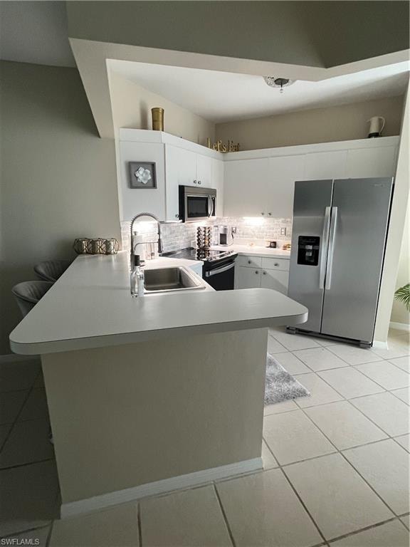 Kitchen featuring white cabinetry, stainless steel appliances, a white subway tile backsplash, and a breakfast bar with an integrated sink