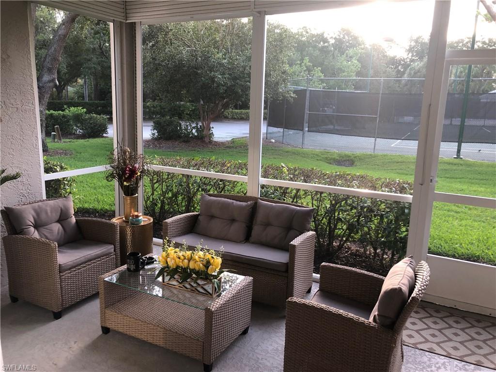 Screened patio featuring a concrete floor with a patterned rug, white screen enclosure, and direct access to a tennis court