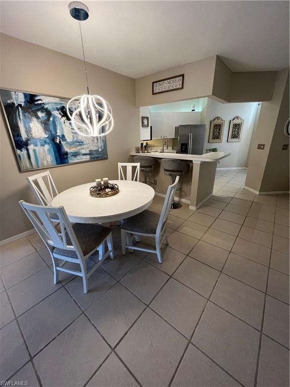 Dining area featuring a contemporary pendant light fixture, tile flooring, and a pass-through opening to the kitchen with a breakfast bar