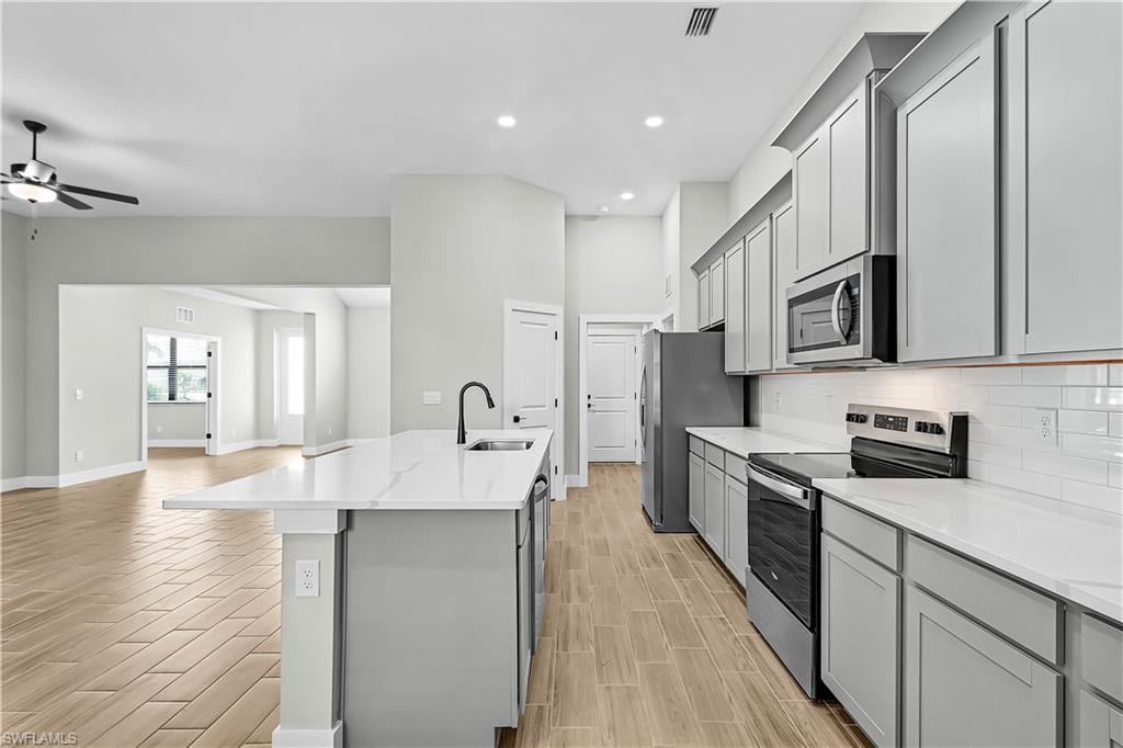 Kitchen with gray cabinetry, stainless steel appliances, open floor plan, wood finish floors, and recessed lighting