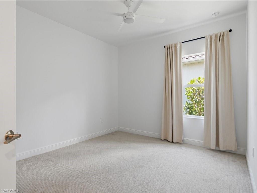 Carpeted interior room featuring a window with natural light, a ceiling fan, and white baseboards