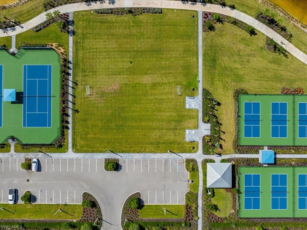 Recreational area featuring multiple sports courts, an expansive grassy field, and paved walking paths