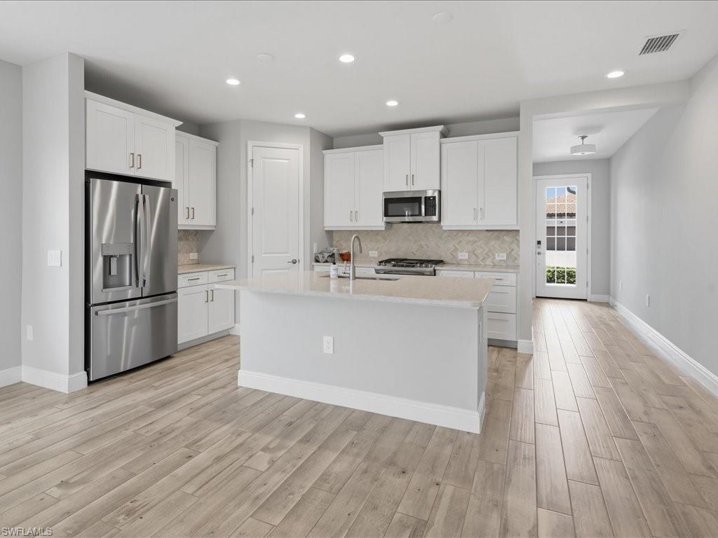 Kitchen featuring white cabinetry, stainless steel appliances, a center island with sink, and a herringbone pattern tile backsplash