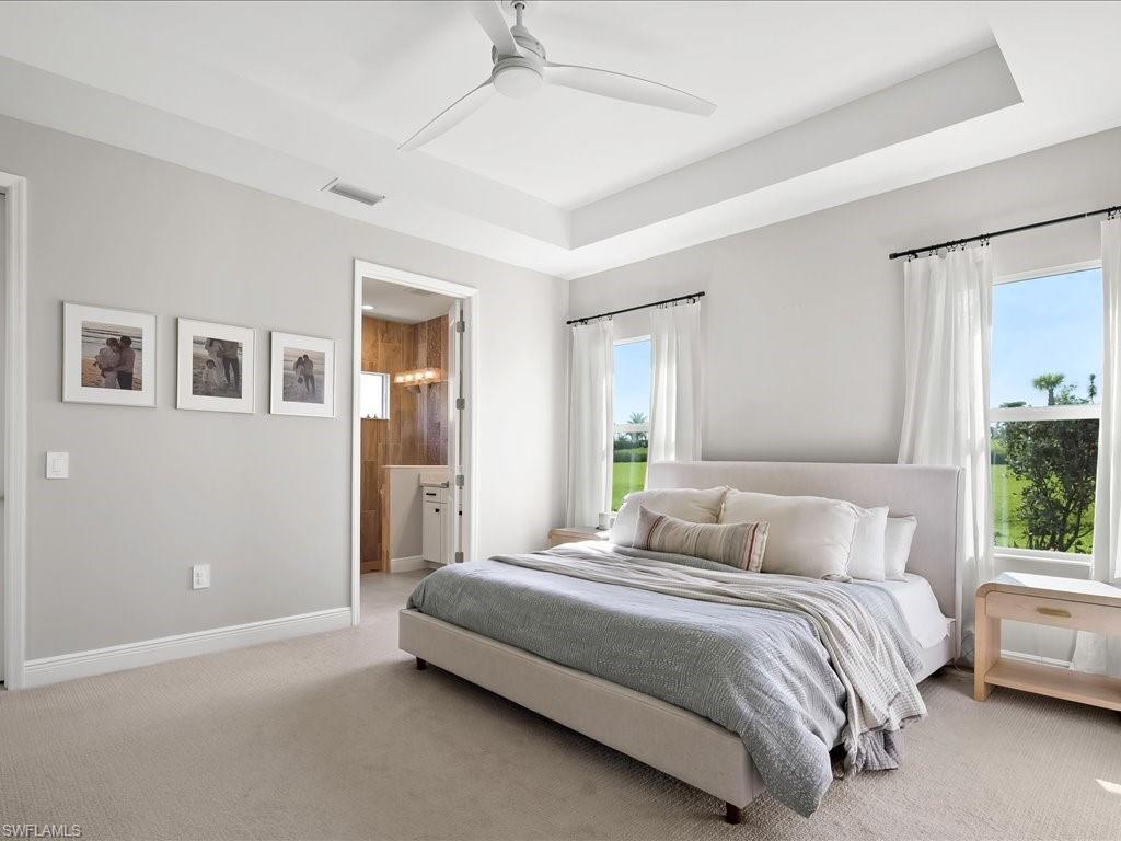 Carpeted bedroom with a tray ceiling and a ceiling fan