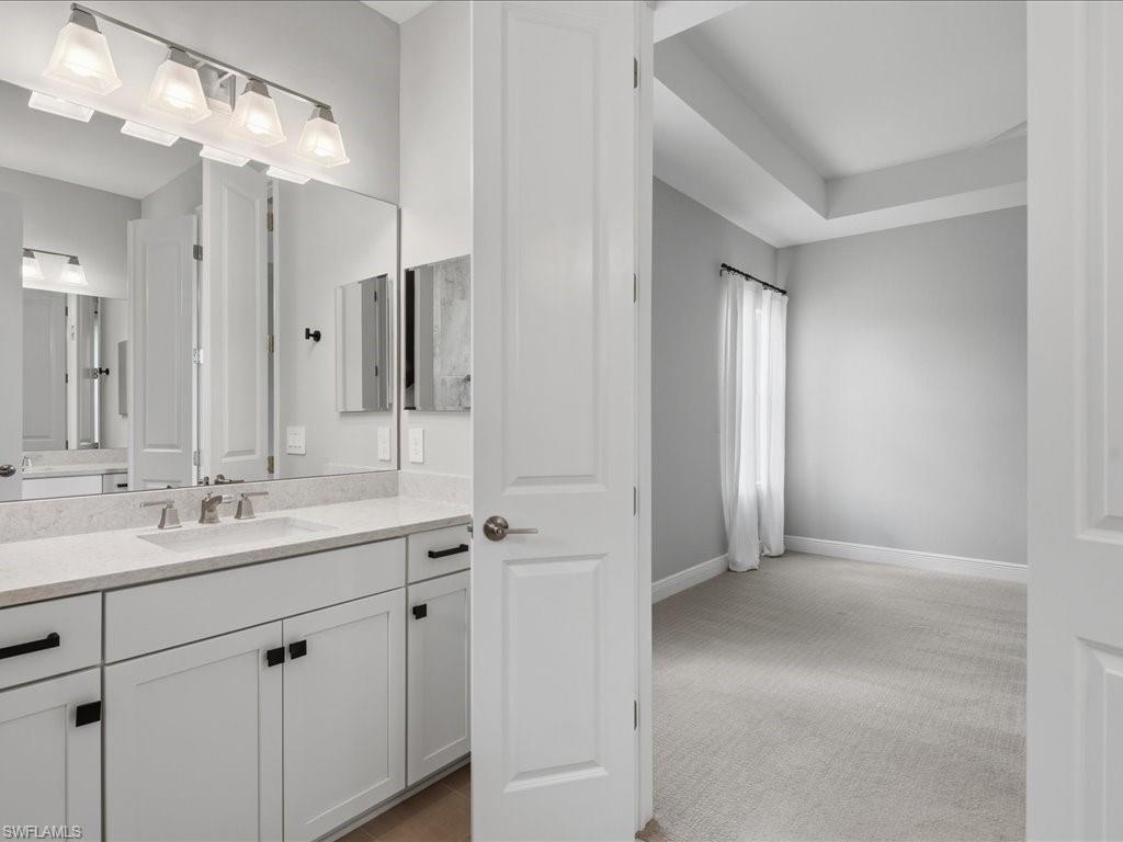 Bathroom vanity with double sinks, light-toned countertop, white cabinetry with black hardware, and a four-light fixture