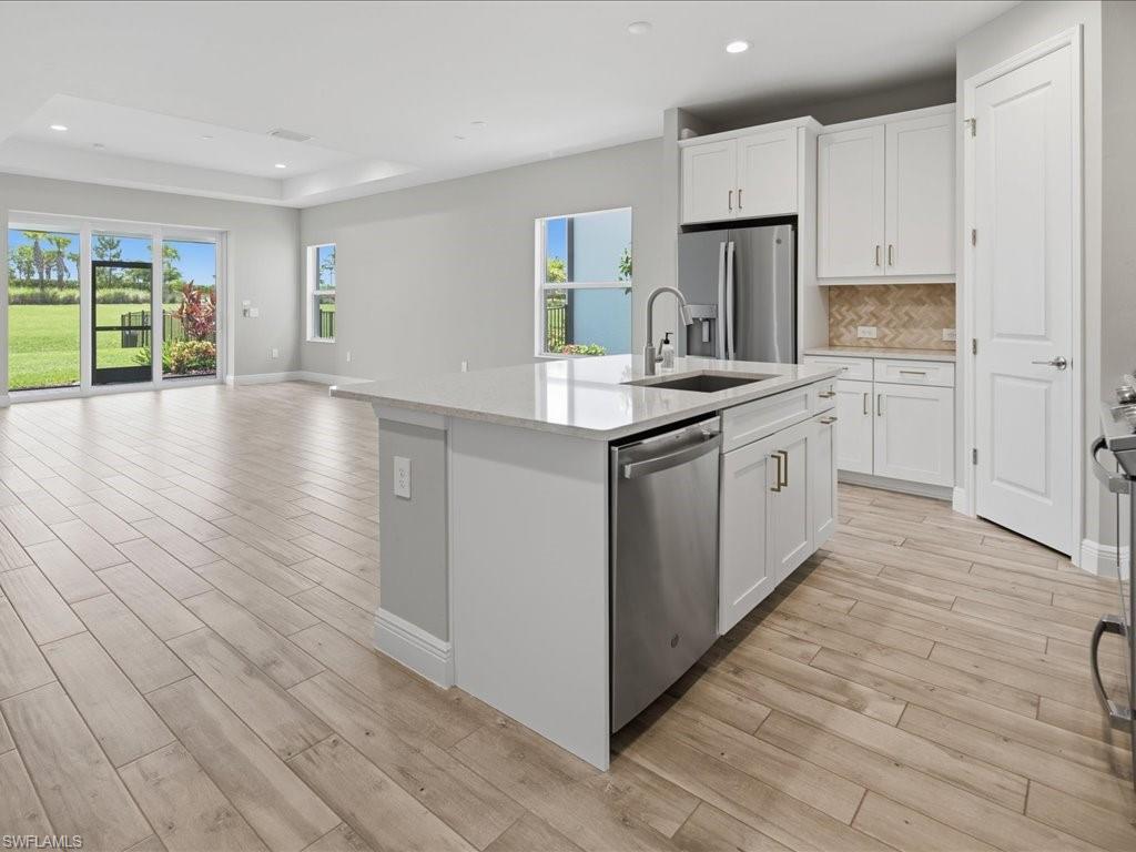 Open-concept kitchen and living area featuring a large center island with a sink, white cabinetry with brushed nickel hardware, and stainless steel appliances