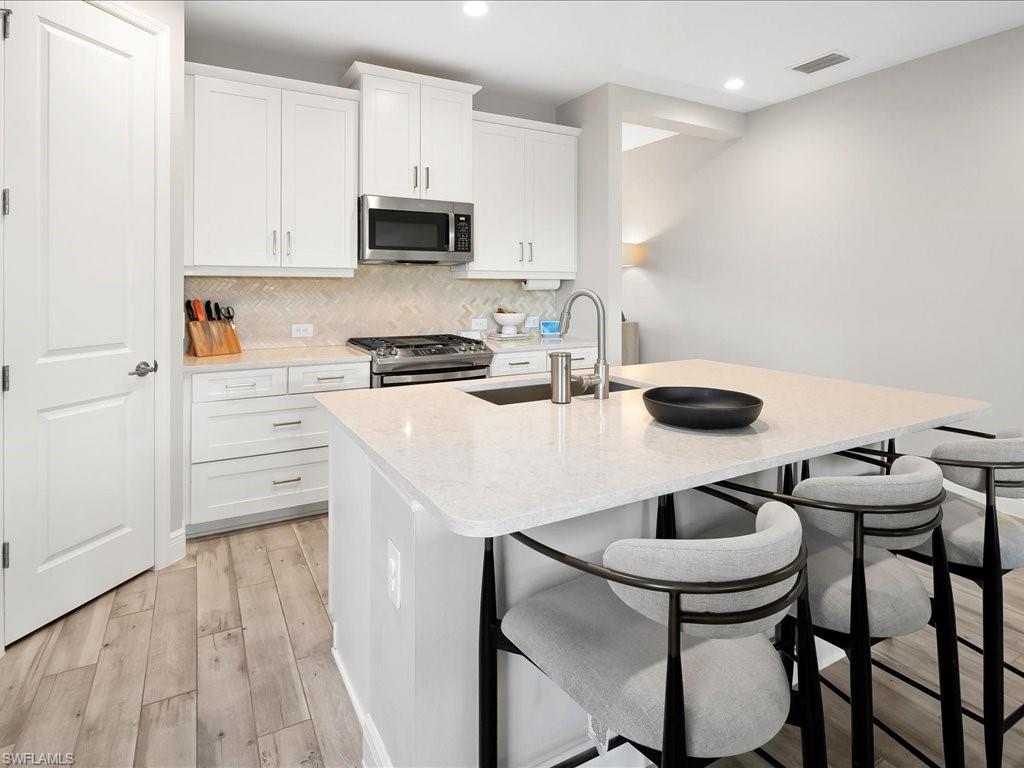 Kitchen featuring a central island with countertop seating, white cabinetry, stainless steel appliances, a herringbone tile backsplash, and wood-finish flooring