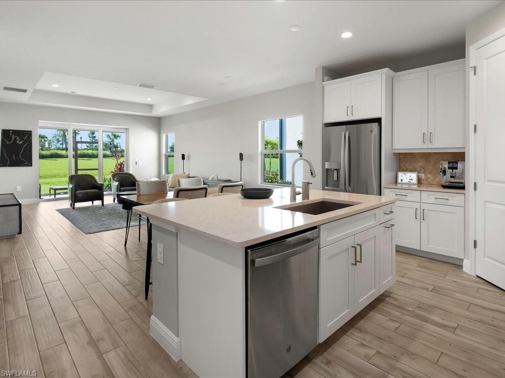 Open-concept kitchen featuring a central island with an undermount sink, light-toned countertop, and white shaker-style cabinetry