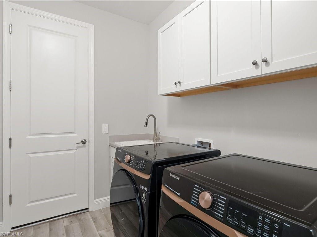 Laundry area featuring wood-finish flooring, white shaker cabinetry, a utility sink with a high-arc faucet, and light gray wall paint