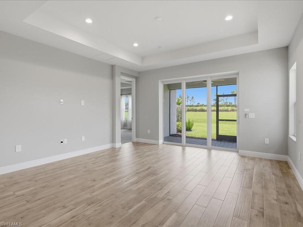 Recessed lighting illuminates a tray ceiling and light-toned wood-finish flooring