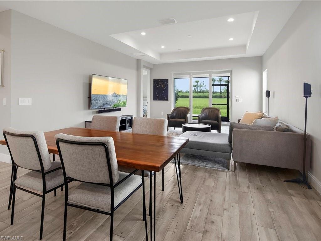 Open-concept living area featuring wood-finish flooring, a tray ceiling with recessed lighting, and expansive glass doors opening to green space