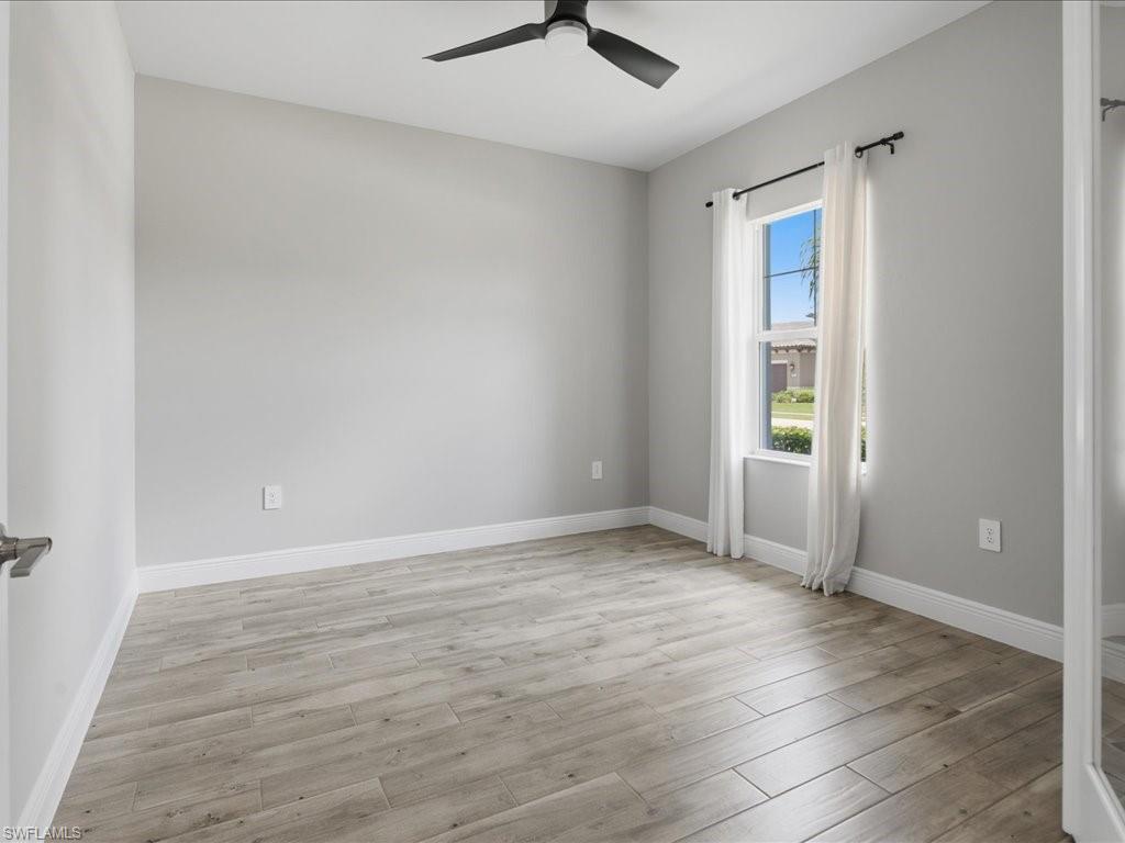 Spacious room featuring light gray walls, wood-finish flooring, a ceiling fan, and a double-hung window
