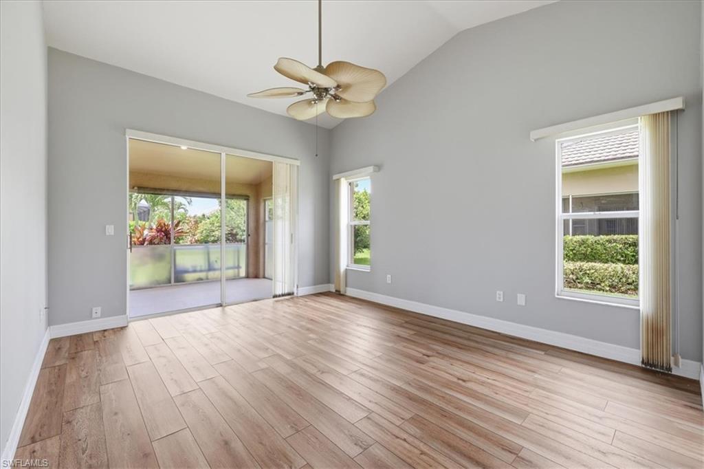 Vaulted ceiling room featuring wood-finish flooring, a ceiling fan, and sliding glass doors opening to an outdoor patio