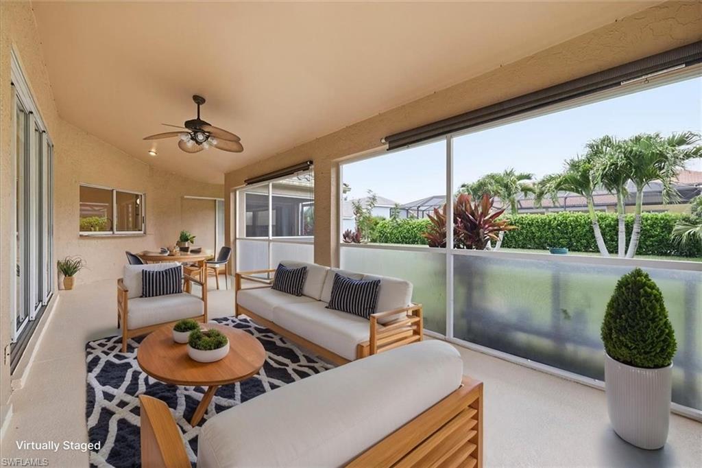 *VIRTUALLY STAGED* Screened lanai featuring a ceiling fan, tiled flooring, an outdoor dining area, and a tropical landscape beyond