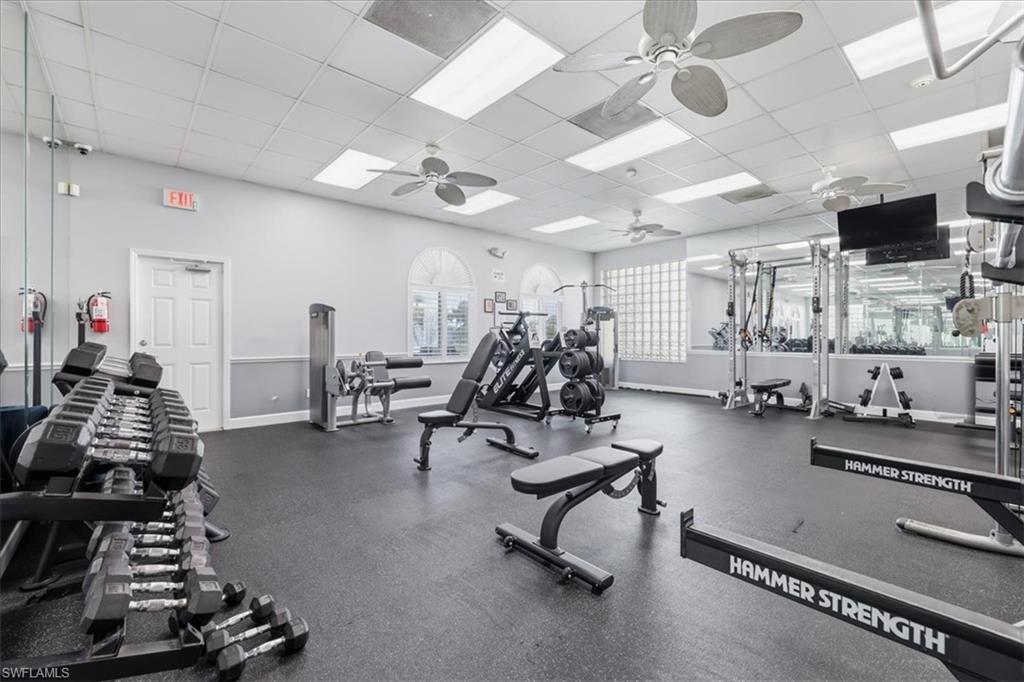 Fitness center featuring rubber flooring, a mirrored wall, arched windows, built-in ceiling lighting, and ceiling fans
