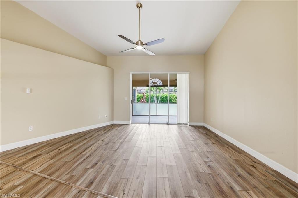 Expansive room featuring wood-finish flooring, vaulted ceilings, and a ceiling fan with integrated lighting