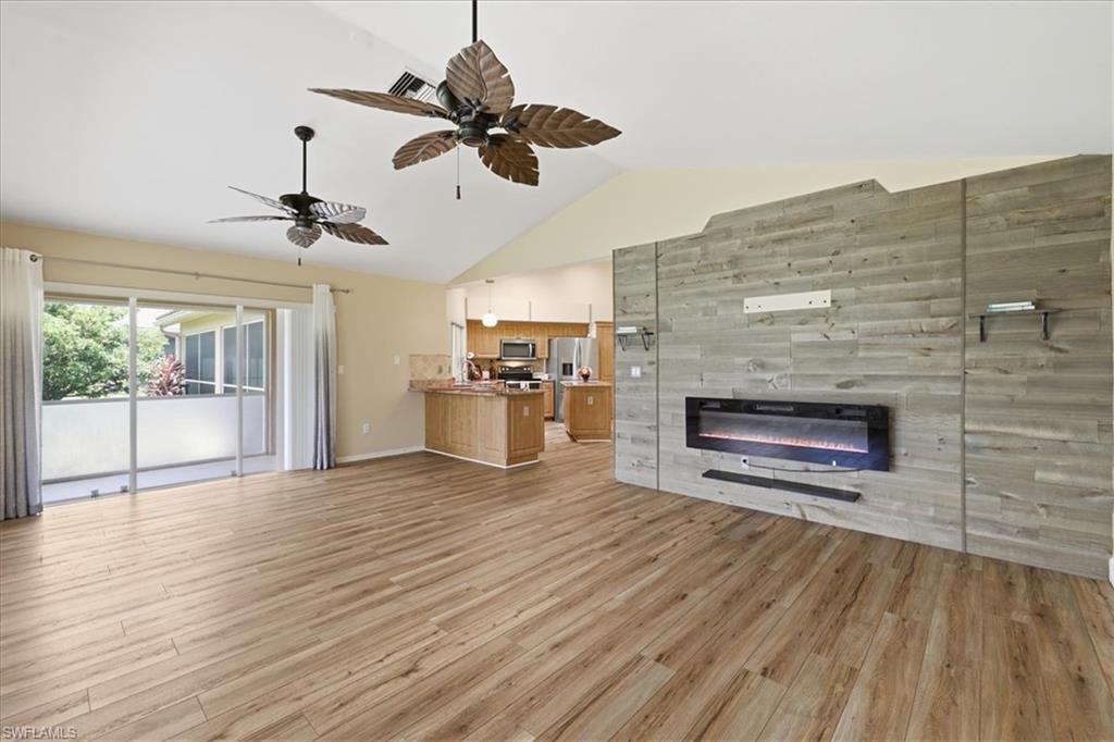 Open-concept living area featuring wood-finish flooring, a vaulted ceiling, and dual ceiling fans