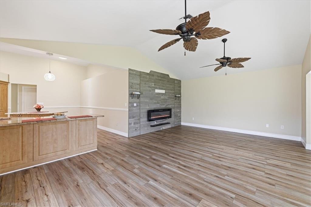 Spacious living area featuring wood-finish flooring, a stone-clad fireplace, and vaulted ceilings