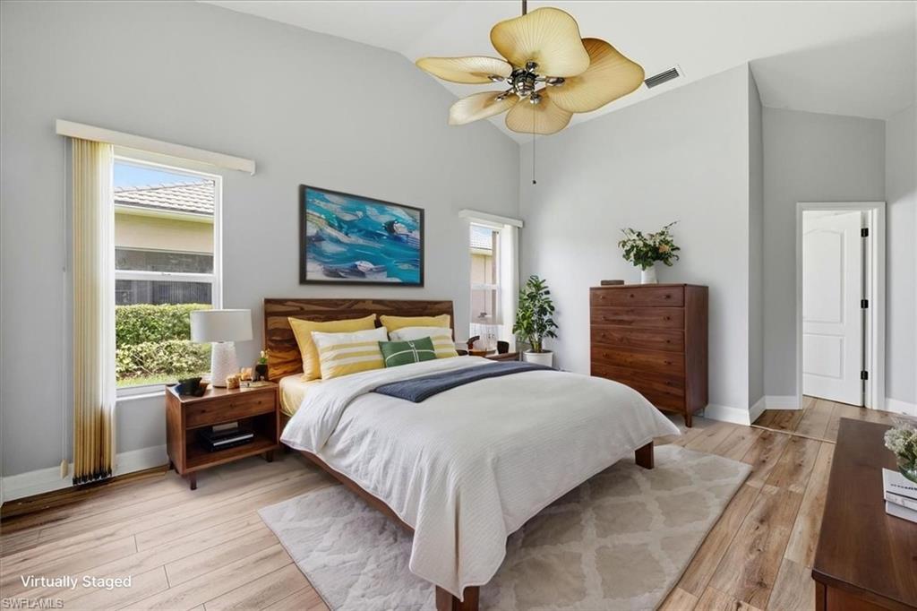 *VIRTUALLY STAGED* Vaulted ceiling bedroom featuring wood-finish flooring, two windows with outdoor scenery, and a tropical-style ceiling fan