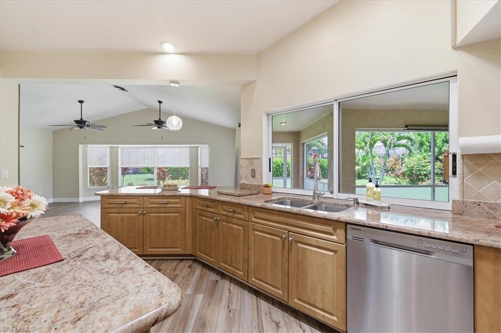 Kitchen featuring light wood cabinetry, stone countertops, stainless steel dishwasher, double basin sink, and a tiled backsplash