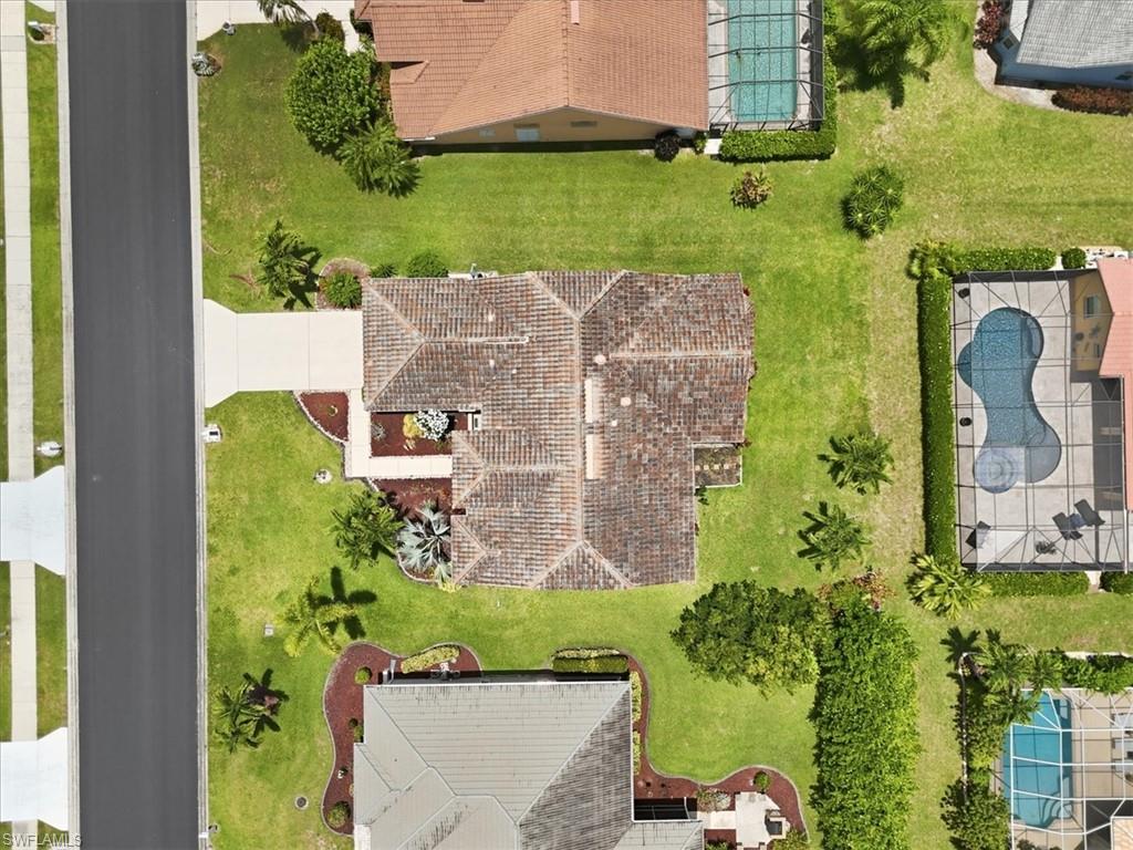 Overhead property view featuring a tile roof, concrete driveway, and front landscaping with mature shrubs