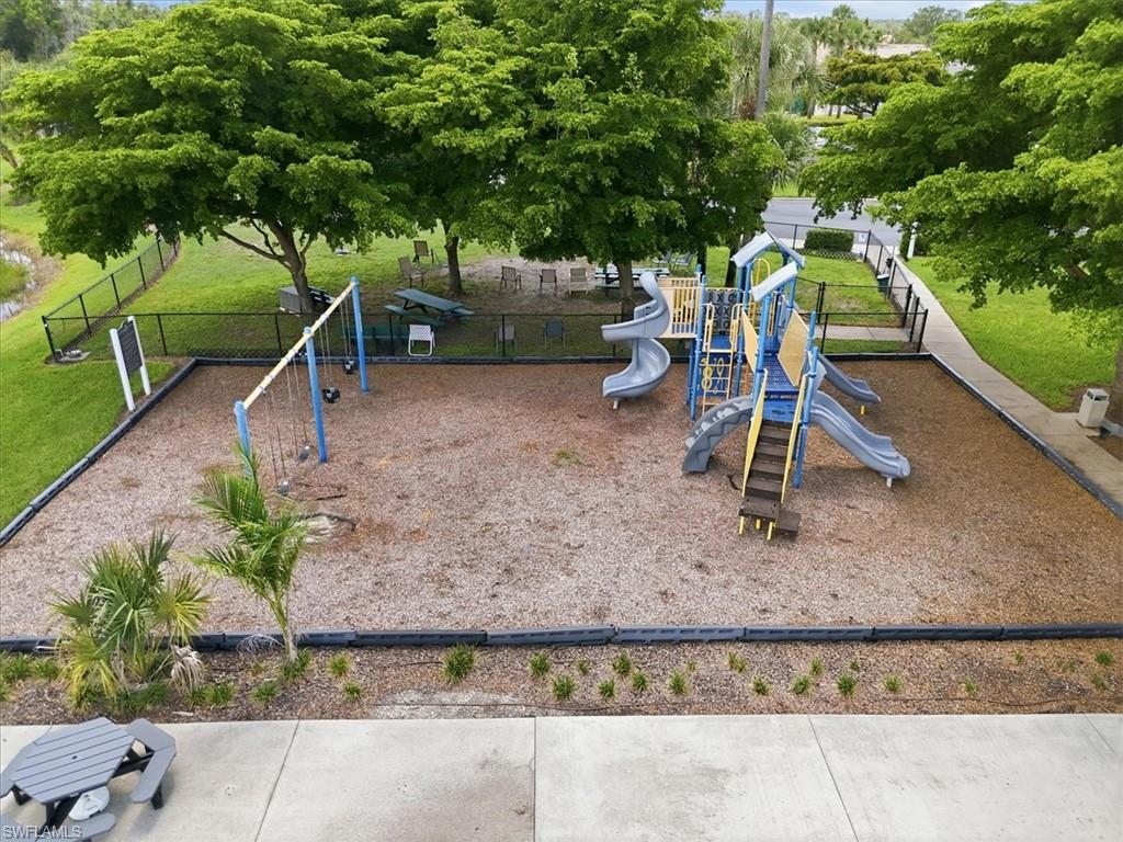 Recreational area featuring a playground with slides and swings, wood chip surfacing, perimeter fencing, and mature trees