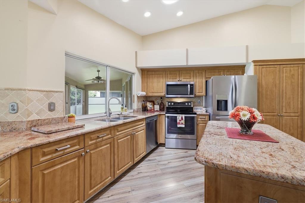 Open-concept kitchen featuring vaulted ceilings, recessed lighting, wood-finish flooring, light wood cabinetry, and extensive granite countertops