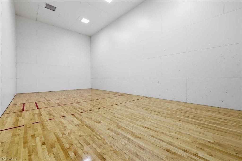 Indoor court featuring wood flooring with red and black court lines, white paneled walls, and recessed ceiling lighting
