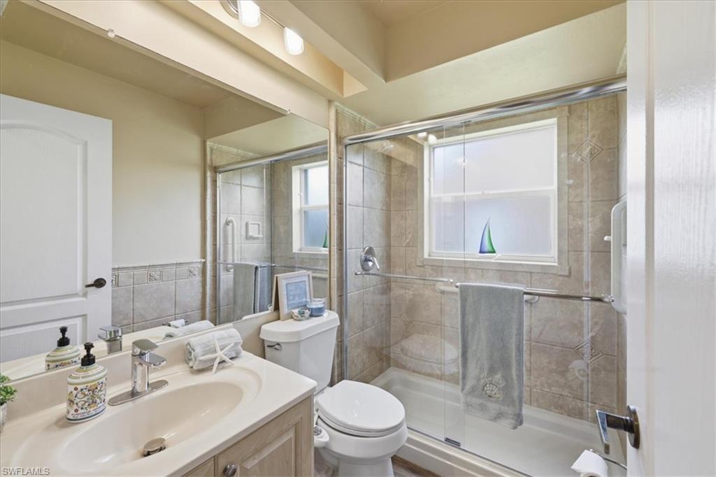 Full bathroom featuring a single vanity with an integrated sink, a toilet, and a tiled shower with a glass enclosure