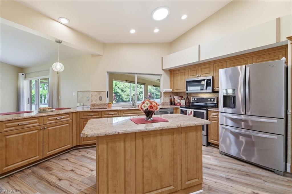Kitchen featuring wood cabinetry, granite countertops, stainless steel appliances, a central island, and wood-finish flooring