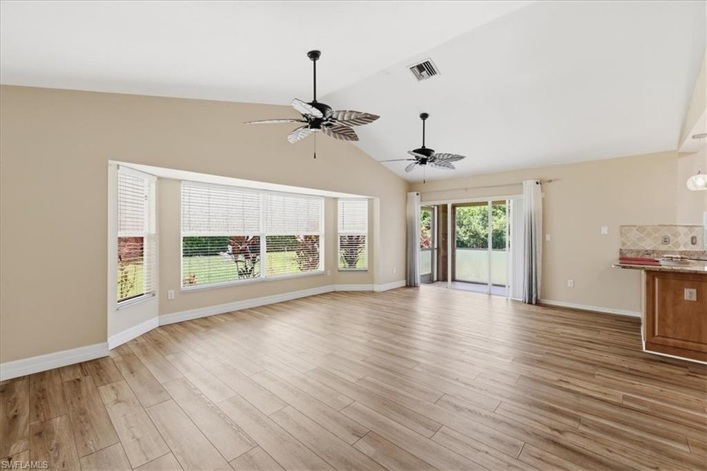Expansive living area featuring vaulted ceilings, wood-finish flooring, and a wide bay window with blinds