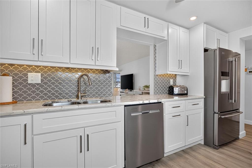Kitchen featuring white shaker cabinetry, stainless steel appliances, marble-look countertops, a scallop-patterned backsplash, and wood-finish flooring