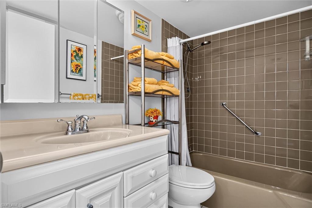 Full Guest Bathroom featuring an integrated sink vanity with white cabinetry, a three-panel mirrored medicine cabinet, a tiled shower surround, and a built-in grab bar