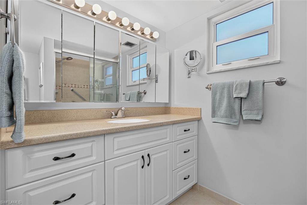 White vanity with recessed paneling and dark hardware, featuring a beige countertop, an integrated sink, and a chrome faucet