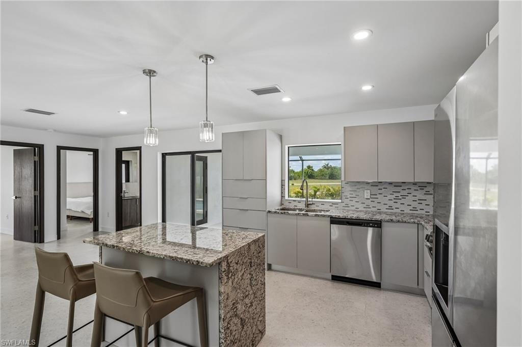 Modern kitchen featuring a granite-topped island with seating, stainless steel appliances, contemporary cabinetry, and a patterned tile backsplash