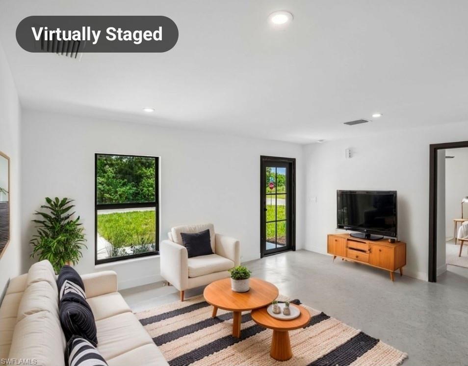 Bright living space featuring light gray flooring, white walls, black trim windows, a black frame exterior door with glass panels, and recessed ceiling lighting