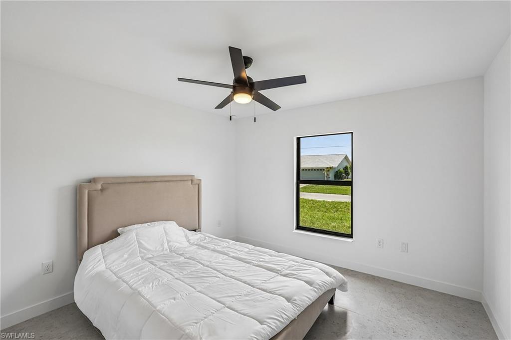 Clean white walls define this room featuring a window with black trim, a ceiling fan with integrated lighting, and polished concrete flooring