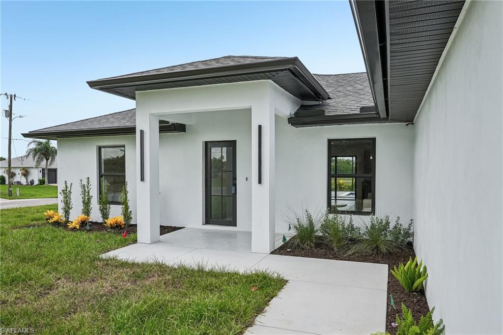 Contemporary exterior featuring a covered entry, dark-framed impact windows, modern vertical lighting fixtures, a dark glass-paneled entry door, and a concrete pathway